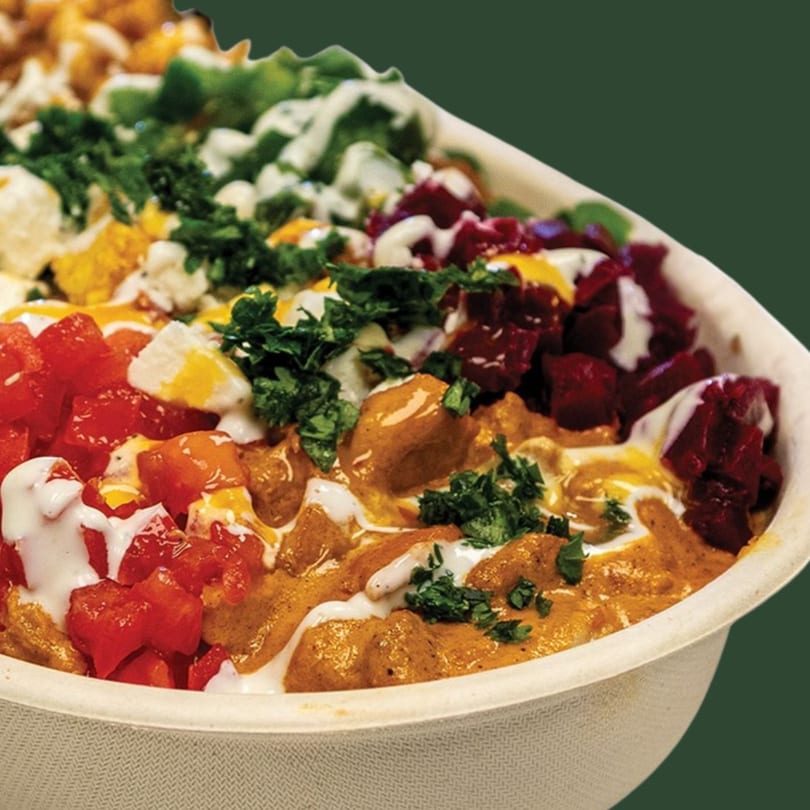 Close-up of a colorful bowl with chicken, diced tomatoes, beets, and green herbs drizzled with sauce.