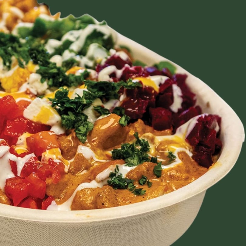 Colorful bowl with chicken, red tomatoes, green herbs, and white sauce, against a dark green background.