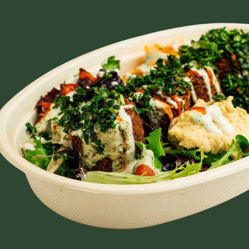 Falafel bowl with hummus, greens, and sauces, garnished with fresh herbs in a white bowl.